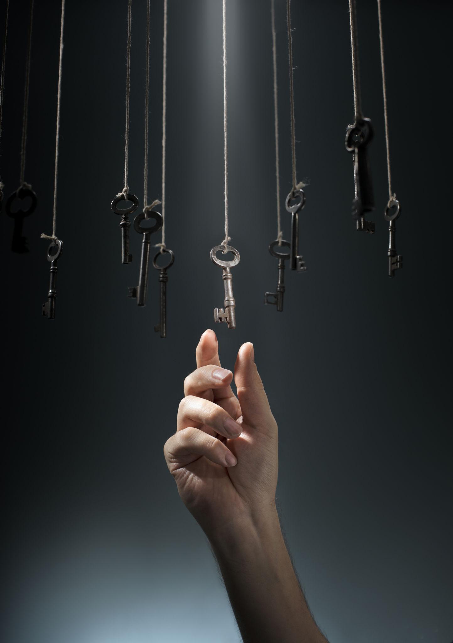 Hand reaching upward toward hanging keys, representing the power of humans having the power to choose.