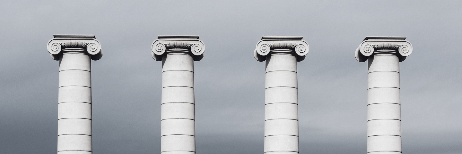 Photo of four pillars standing equidistant from one another against a cloudy gray sky.