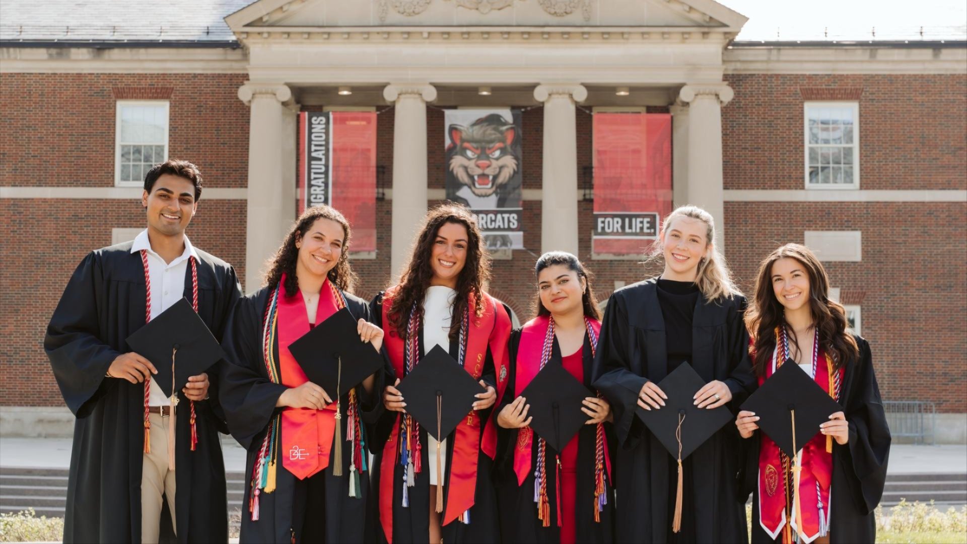 Group of 2026 UC New Grads posting with their caps in front of TUC