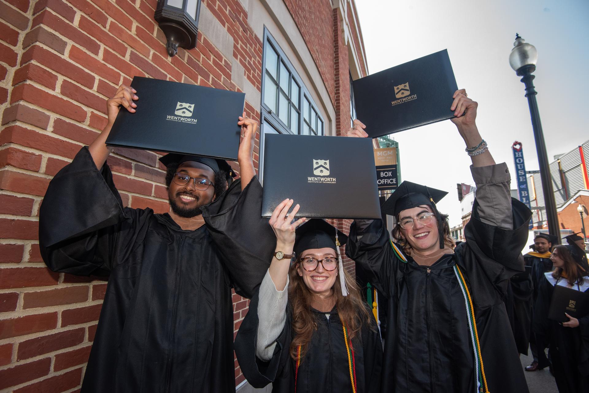 Three students at graduation holding diplomas in the air
