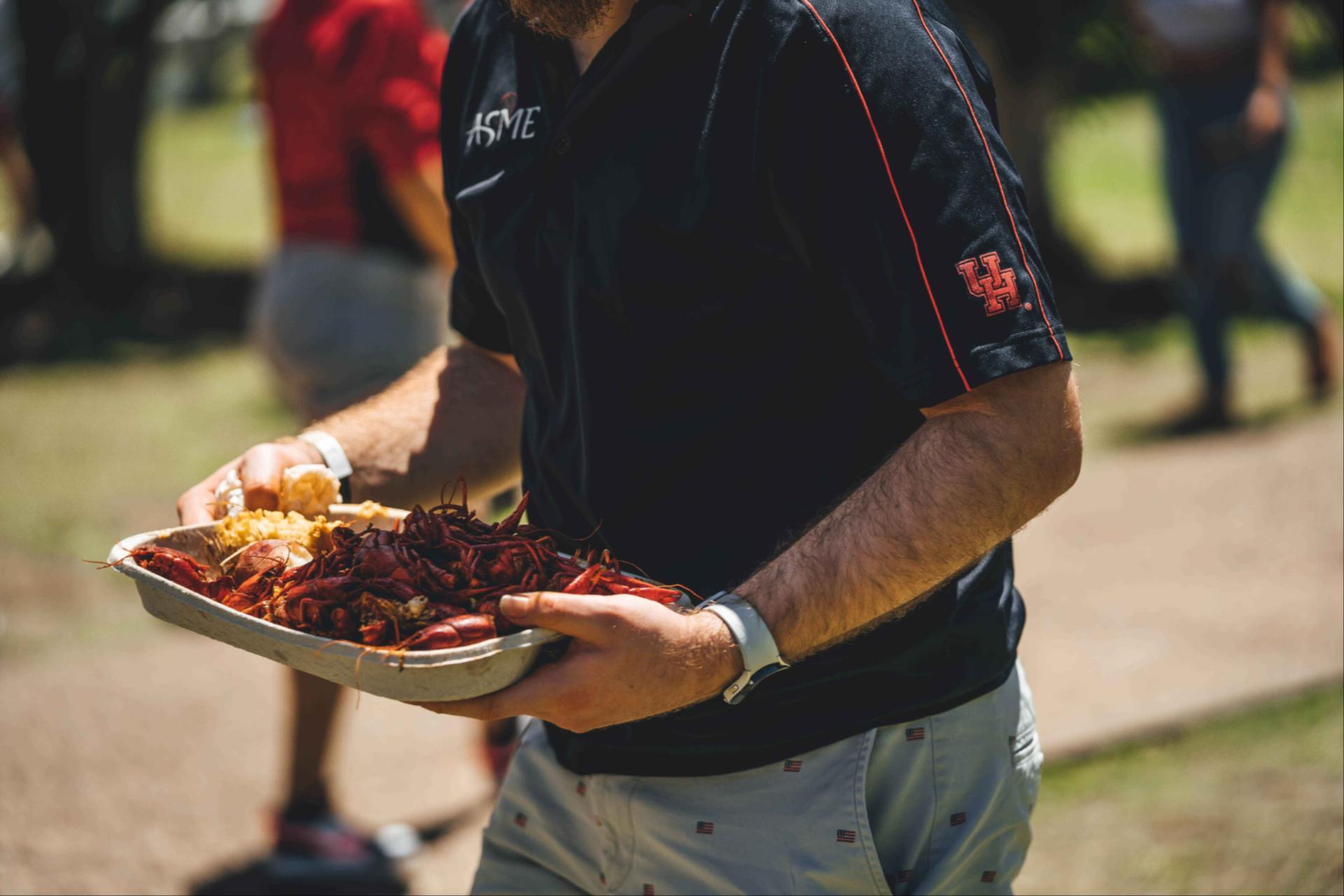 Image of a man holding a tray of crawfish with corn.