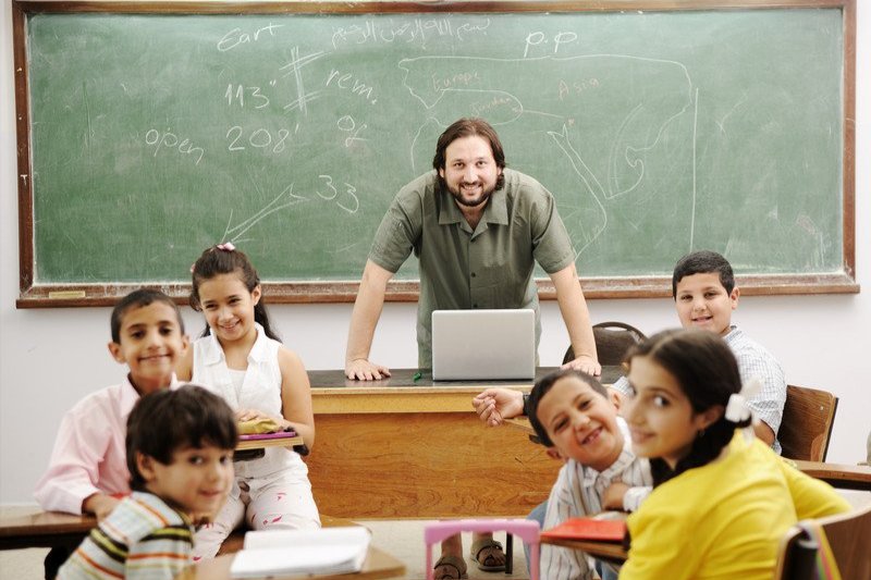 a teacher standing in front of a classroom with children