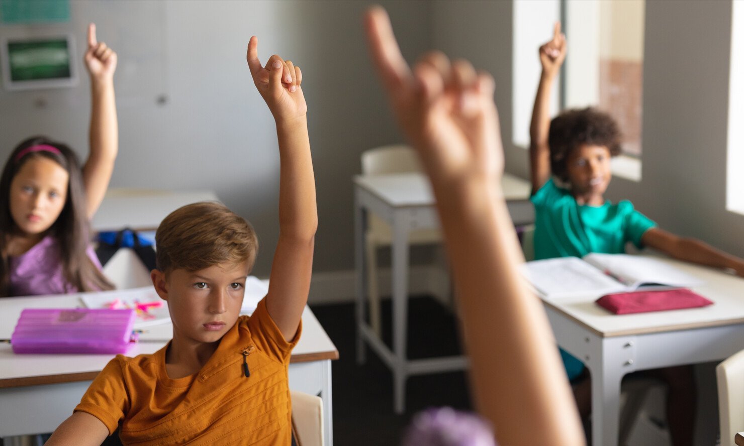 a group of kids raising their hands in a classroom