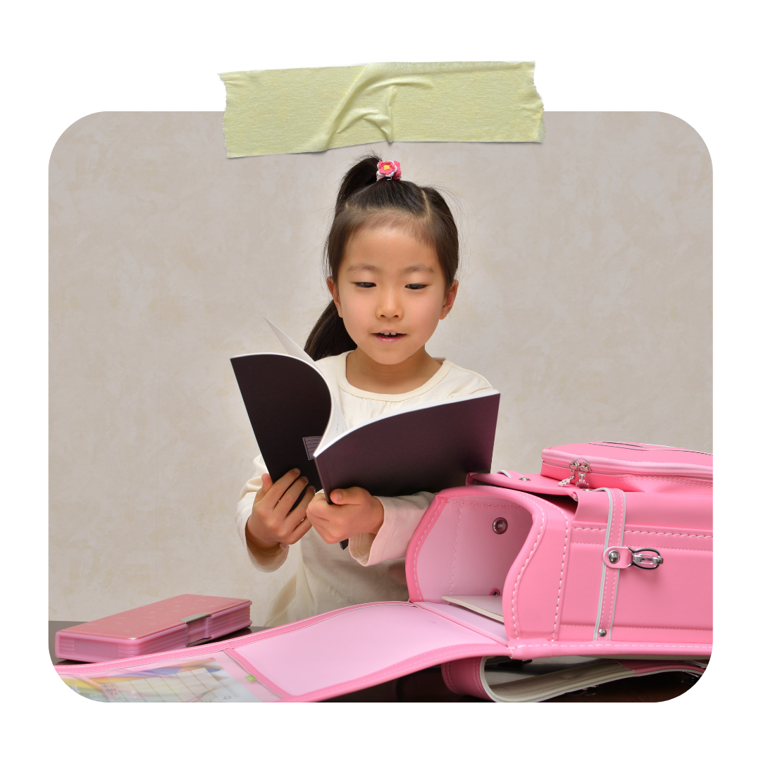 Japanese elementary school girl studying beside a pink randoseru